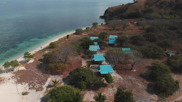 Aerial drone shot of the island house's roofs surrounded of amazing turquoise ocean water with coral reefs and nature. Kanawa island, Indonesia.