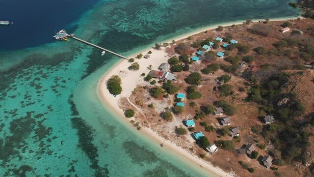 Aerial drone shot of a small island surrounded of amazing turquoise ocean water with coral reefs and some boats in the background. Kanawa island, Indonesia.