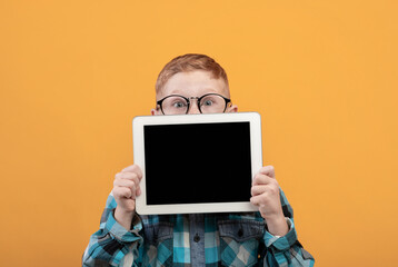 Amazed kid hiding behind digital tablet with empty screen