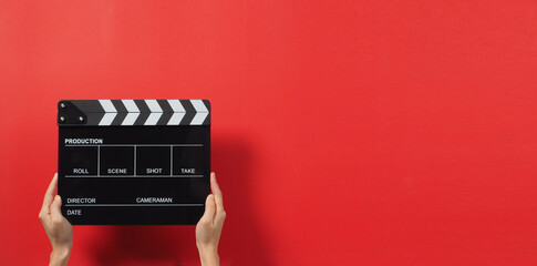 Hand is holding black Clapper board or Clapperboard or movie slate. it use in video production ,film, cinema industry on red background.