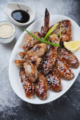 White plate with teriyaki chicken wings, vertical shot on a dark grey stone background