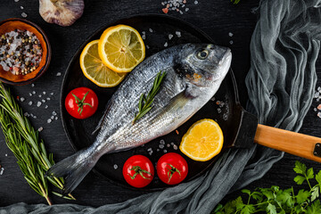 Raw dorado fish and spices for cooking it in a frying pan on a black background, top view