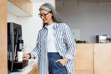 Happy white-haired mature woman smiling while using coffee maker