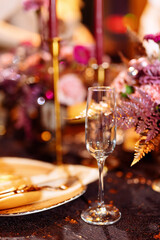 Fototapeta na wymiar Table served for Christmas dinner, festive setting with decorations, burning candles and golden fern branches, glasses. Selected focus and blurred background