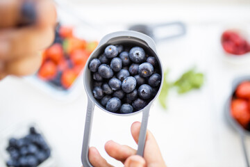 Female hand holding measuring cup full of blueberries above more berries