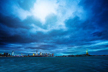 Wide dramatic panorama of the Statue of Liberty over the New York cityscape at the evening dusk and...