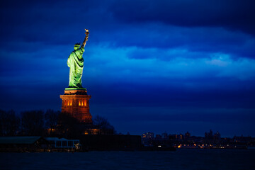 The Statue of Liberty over the New York cityscape from Black Tom Island at night illuminated with light © Sergey Novikov