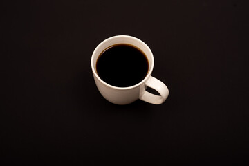 Obraz na płótnie Canvas Top view of white ceramic mug with black coffee on black background.