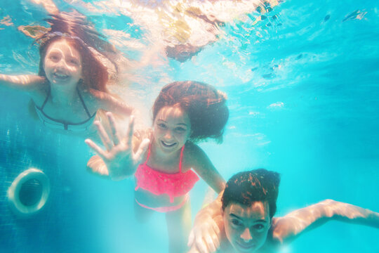 Group of three friends children dive underwater together waving hands and smiling