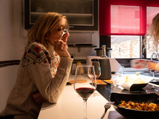 BLONDE WOMAN IN NICE KITCHEN DRINKING A GLASS OF WINE WHILE SNACKING SOMETHING