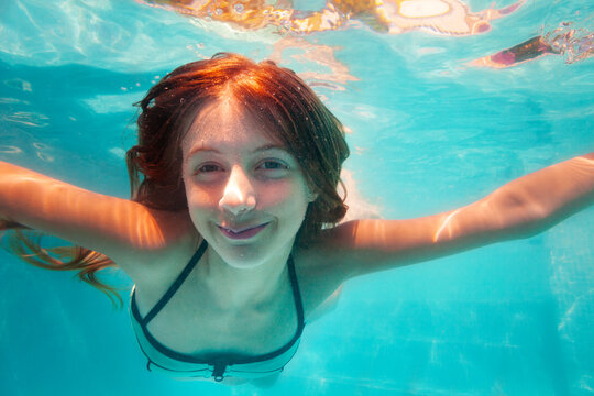 Happy friendly close portrait of the girl stretch hands, smile and swim underwater in the pool