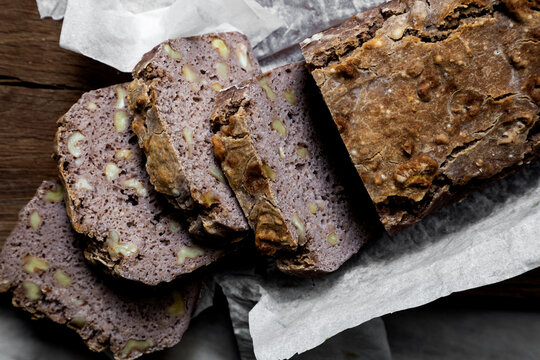 Handcrafted gluten free sourdough bread with buckwheat and walnuts on a wooden cutting board placed on white marble countertop