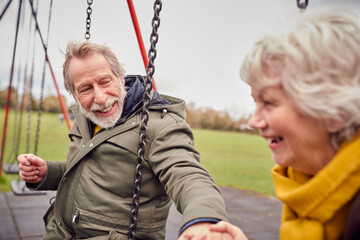 Obraz premium Senior Couple Having Fun Playing On Swings In Park Playground