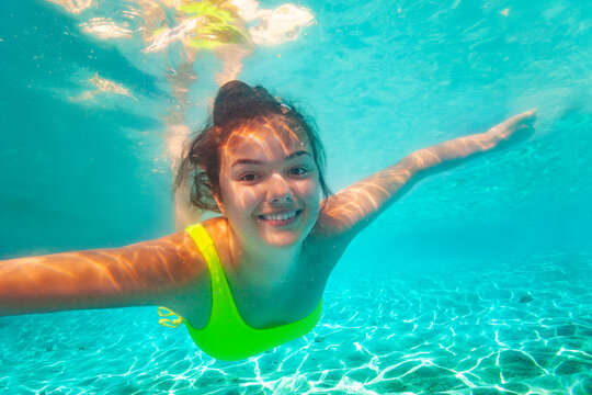 Portrait of happy teen smiling positive girl with screaming open mouth and spread hands floating swimming underwater in the sea