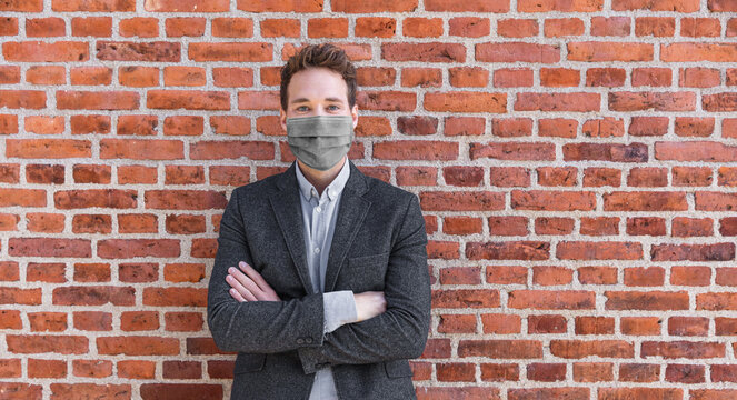 Man businessman confident portrait wearing face mask for coronavirus prevention in urban city brick background. Crossed arm entrepreneur or realtor.