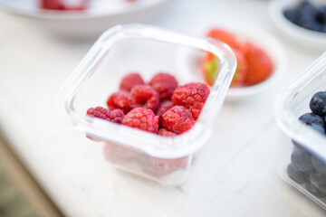 Raspberries in a plastic container on a white table