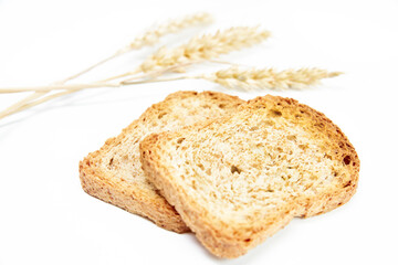 Two crusty bread toast slice next to ears of wheat on white background