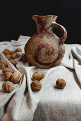 Vintage clay pot on black background and linen texture with walnuts.