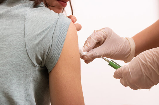 Hands of a doctor with a syringe and cotton wool to disinfect the injection site, injecting the vaccine into the hand of a teenager in a clinic on a white background. 