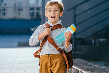 Cute blond little boy going first time to school. Pupil of primary school take backpack at sunny day outdoor.