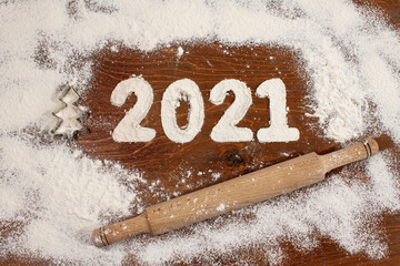 the inscription 2021 is made of flour on a wooden table, white flour is scattered around and there...