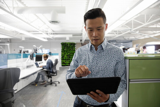 Man Leaning On Office Partition Using Digital Tablet