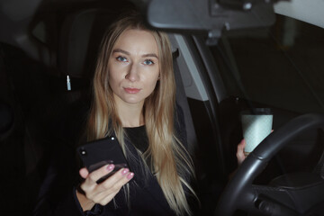 Young woman drinking coffee and typing on the phone in the car