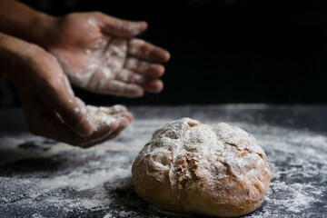Fototapeta premium Bread baking concept.Hands with flour and traditional bread on floury table with black background.Copy space.