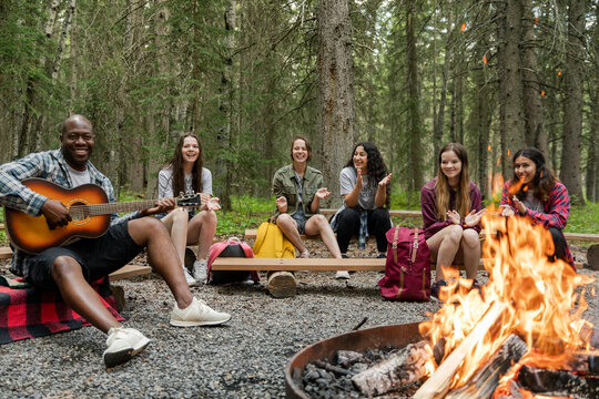 Man playing guitar to girls by campfire
