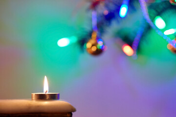 Obraz na płótnie Canvas The flame of a candle stands on the table against a background of blurry Christmas lights. New Year card. Selective focus, blurred background.
