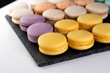 Macarons are laid out on a black slate in beautifully colored rows.