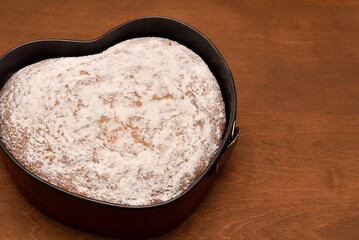 heart shaped cake dusted with powdered sugar in springform pan on a wooden table