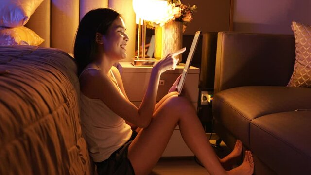 Young Asian beautiful sexy woman  using smartphone- tablet  enjoy  social online and facetime and listening music on bed with happy and smile in bedroom at night time.
