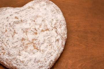 heart shaped cake, freshly baked and dusted with powdered sugar, top view on a wooden table background