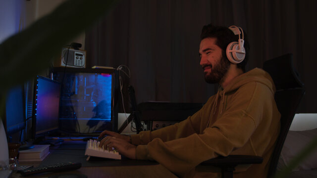 Male using PC and concentrating while wearing white headphones in a darkened room