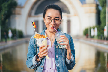 Happy Asian woman enjoying refreshing beverages and eating Belgian fries while looking at the camera