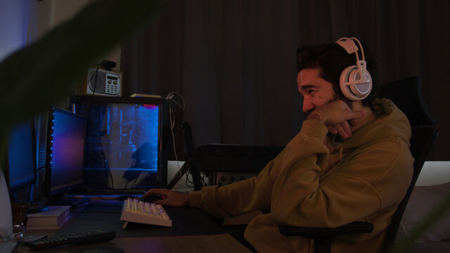 Male using PC and concentrating while wearing white headphones in a darkened room
