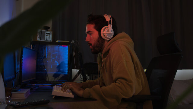 Male using PC and concentrating while wearing white headphones in a darkened room