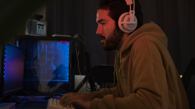 Male using PC and concentrating while wearing white headphones in a darkened room