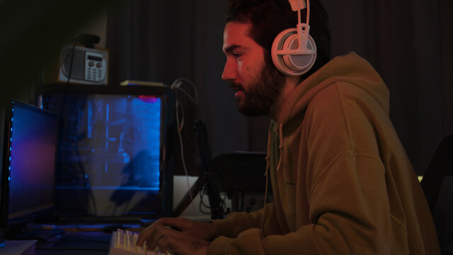 Male using PC and concentraiting while wearing white headphones in a darkened room