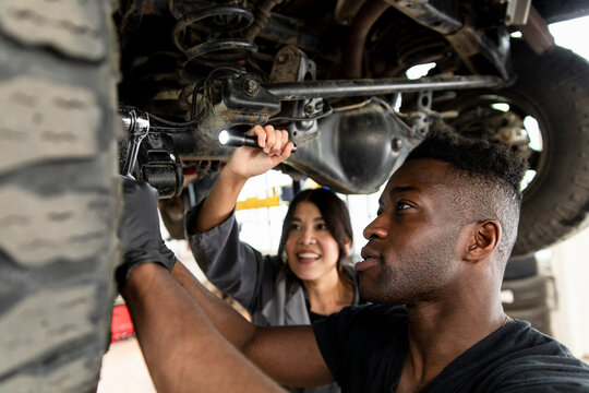 Auto Mechanics Working Under Car On Hydraulic Lift In Garage