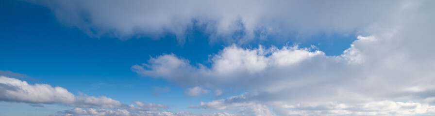 Blue sky with clouds in sunlight, wide cloudscape background panorama