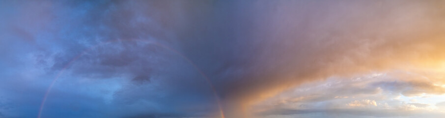 Summer sunset after rain sky panorama with fleece purple clouds and rainbow. Evening dusk good weather natural cloudscape background.