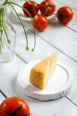 piece of cheese with tomatoes on a wooden board, cheese samples, cheese with a cut on a white...