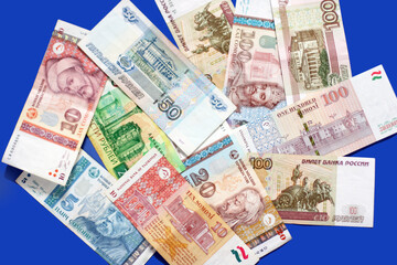 Photo of somoni bank notes from Tajikistan and Russian ruble bank notes on blue background. 