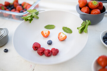 Smiling face made with berries and mint leaves on a plate