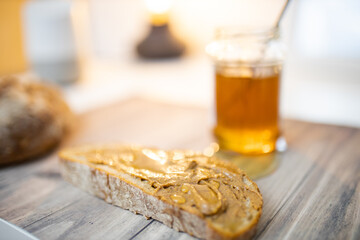 Slice of bread with peanut butter and a honey jar on wooden table