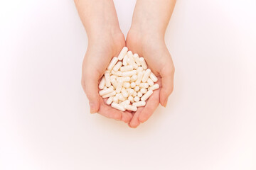 Many white pills are held in two female palms aligned. Close-up, selective focus.