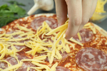 Fototapeta na wymiar Cooking pizza. hand woman cook pouring grated cheese on dough. making Italian pizza