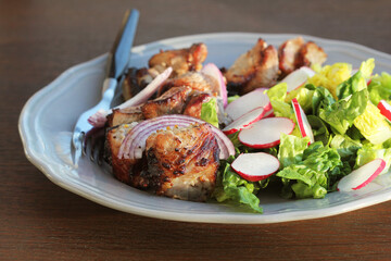Grilled meat kebab and healthy vegetable salad of fresh radish, onion, lettuce on brown background